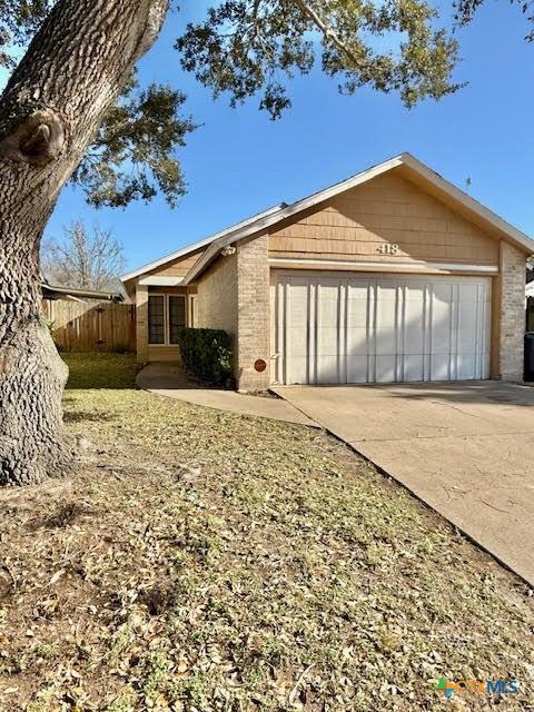 view of home's exterior with driveway, brick siding, an attached garage, and fence