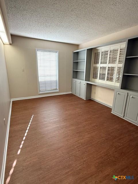 interior space featuring a textured ceiling, wood finished floors, and baseboards