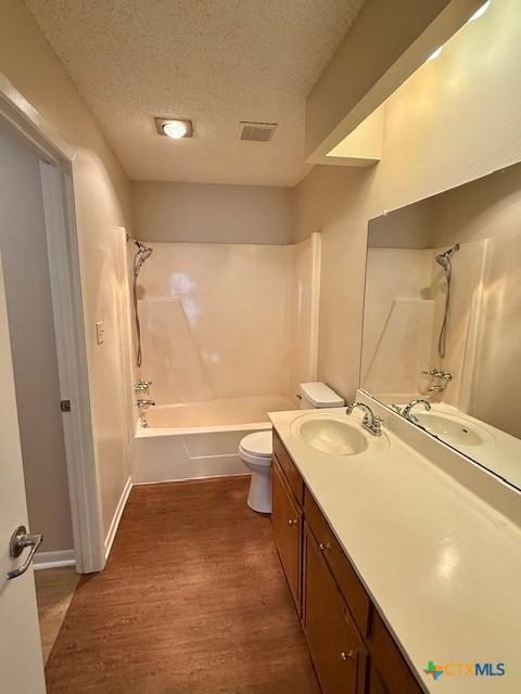 bathroom featuring shower / bathtub combination, toilet, vanity, a textured ceiling, and wood finished floors