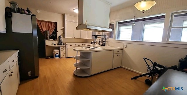 kitchen with stainless steel refrigerator, ventilation hood, light hardwood / wood-style floors, white cabinets, and decorative light fixtures