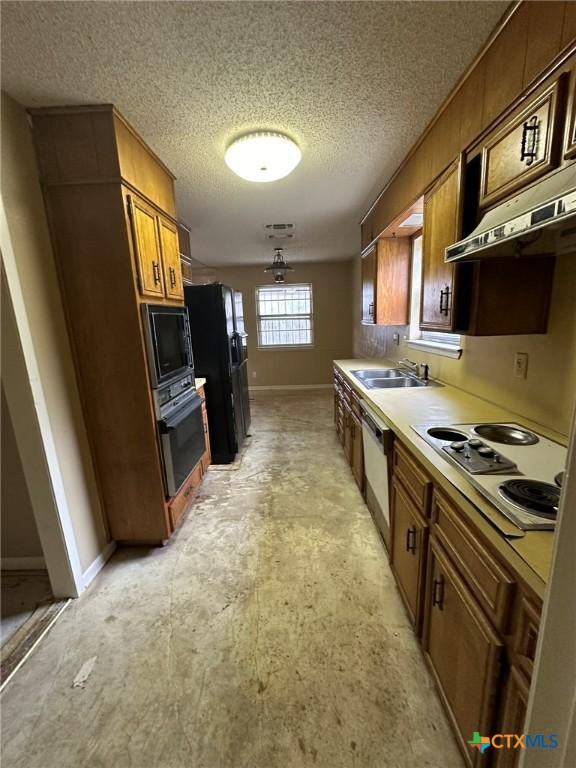 kitchen featuring a sink, black appliances, under cabinet range hood, a textured ceiling, and brown cabinets