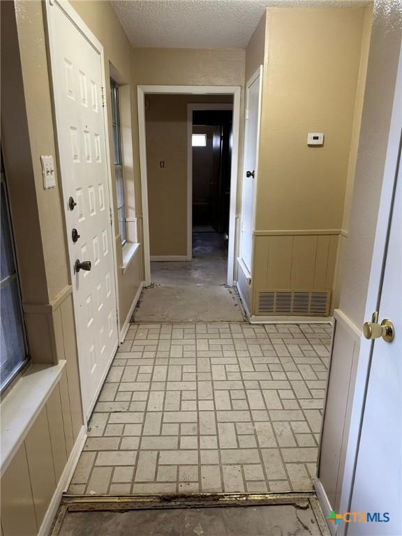 interior space featuring visible vents, a textured ceiling, brick floor, and baseboards