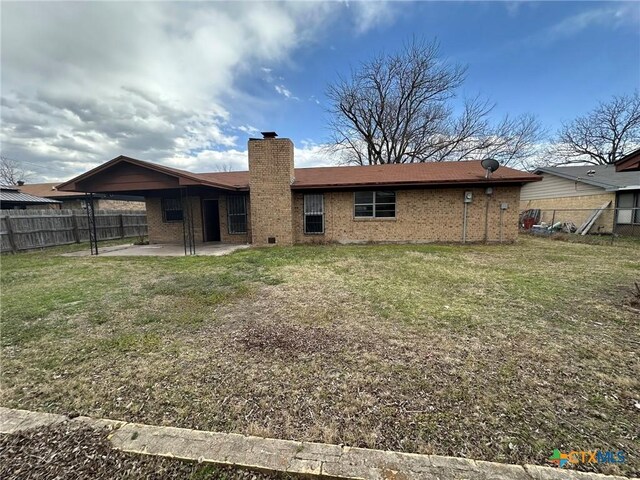 back of house with a lawn, a patio, fence, brick siding, and a chimney