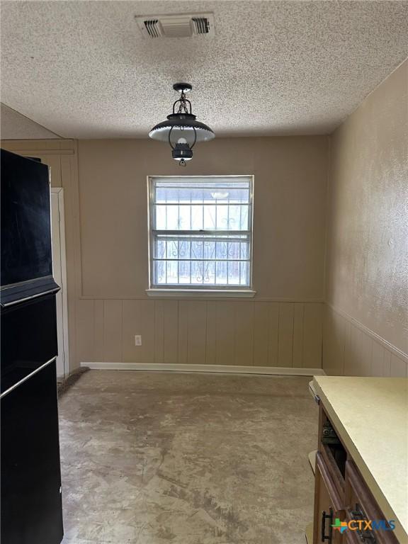 unfurnished dining area featuring visible vents, a textured ceiling, concrete floors, and a wainscoted wall