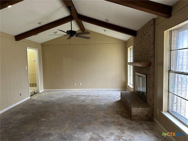 unfurnished living room with unfinished concrete flooring, a textured ceiling, baseboards, a brick fireplace, and vaulted ceiling with beams