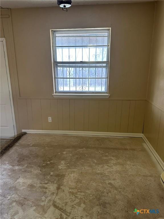 spare room featuring unfinished concrete flooring and wainscoting