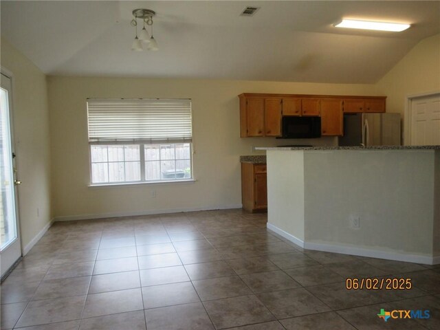 517 Crazy Horse Cir, Harker Heights, TX 76548 - kitchen featuring vaulted ceiling, black microwave, freestanding refrigerator, light tile patterned floors, and brown cabinets