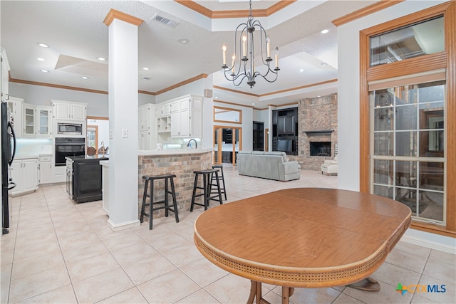 tiled dining area with a chandelier, a raised ceiling, a large fireplace, and crown molding