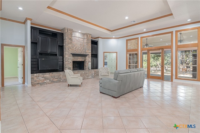 living room with light tile patterned flooring, ceiling fan, a fireplace, a raised ceiling, and crown molding