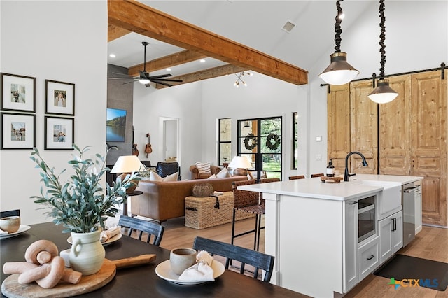 kitchen featuring white cabinetry, a breakfast bar area, a kitchen island with sink, a barn door, and pendant lighting