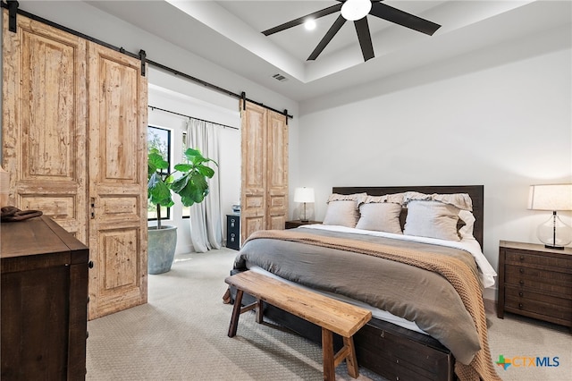 bedroom with light colored carpet, a barn door, ceiling fan, and a raised ceiling