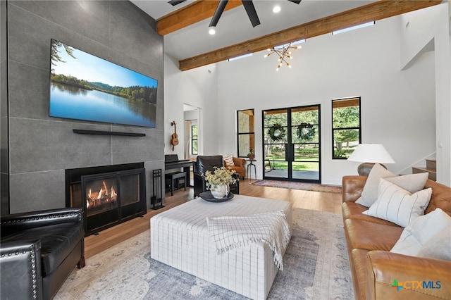 living room featuring ceiling fan, beam ceiling, high vaulted ceiling, a tile fireplace, and light wood-type flooring