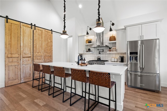 kitchen with white cabinetry, appliances with stainless steel finishes, hardwood / wood-style floors, a barn door, and pendant lighting