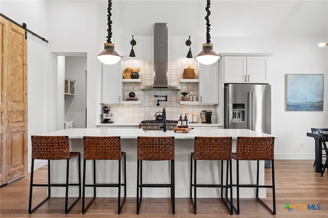 kitchen featuring pendant lighting, a barn door, wall chimney range hood, and white cabinets