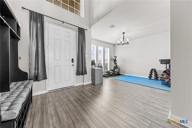 workout room featuring light wood-type flooring, visible vents, a notable chandelier, and baseboards