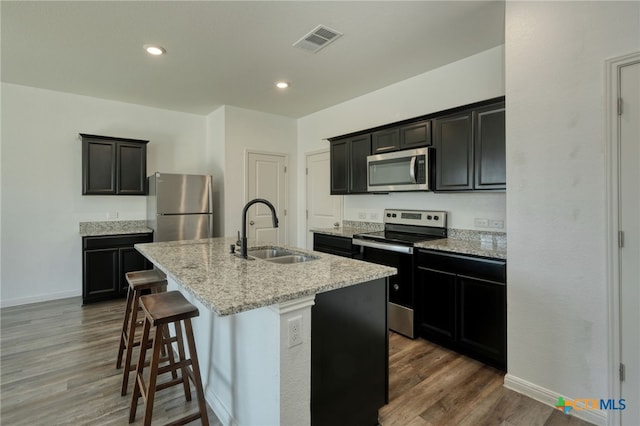 kitchen featuring visible vents, a sink, appliances with stainless steel finishes, wood finished floors, and a kitchen island with sink