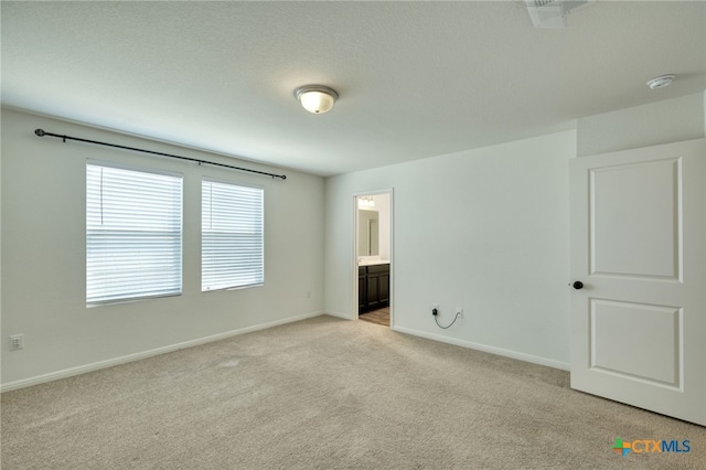 unfurnished bedroom with light colored carpet, ensuite bathroom, and baseboards