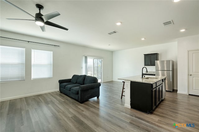 kitchen featuring visible vents, a sink, a kitchen breakfast bar, open floor plan, and freestanding refrigerator