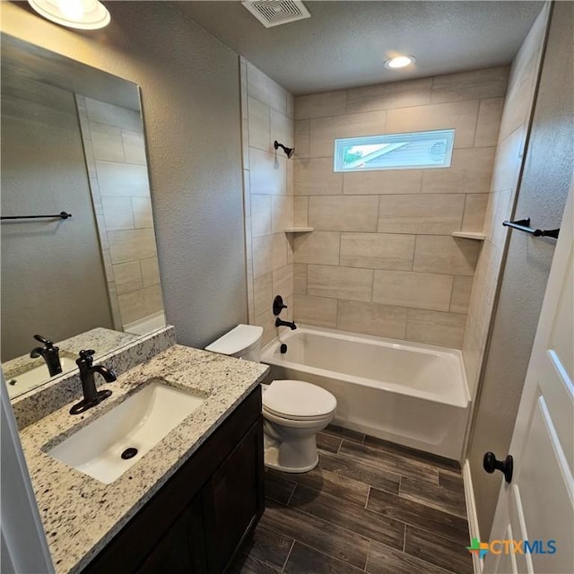 bathroom featuring toilet, wood finish floors, vanity, shower / washtub combination, and a textured wall