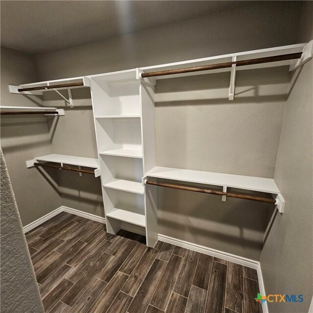 walk in closet with dark wood-style floors