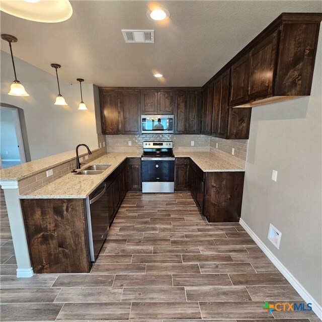 kitchen with light stone counters, stainless steel appliances, pendant lighting, sink, and kitchen peninsula