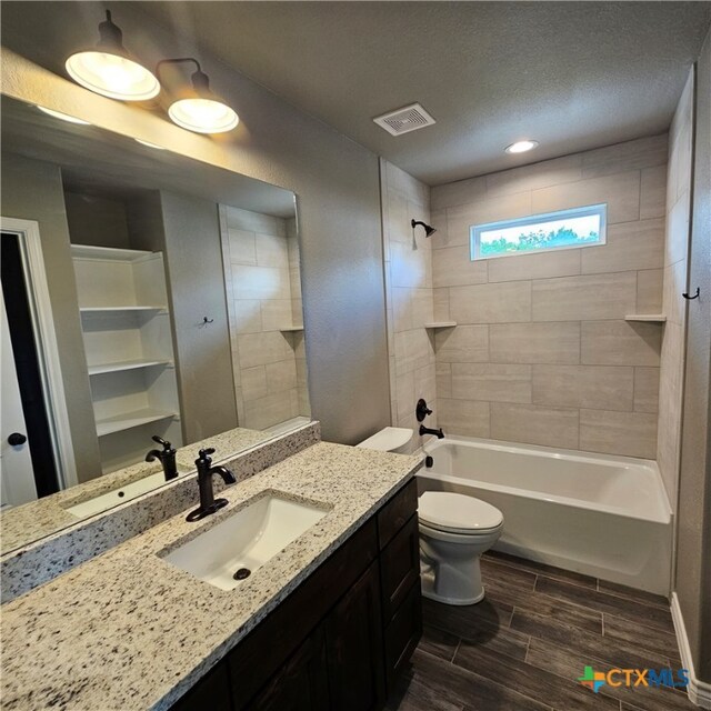 full bathroom featuring vanity, toilet, a textured ceiling, and tiled shower / bath combo