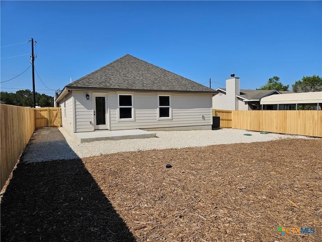 rear view of house featuring a shingled roof, a patio, and a fenced backyard