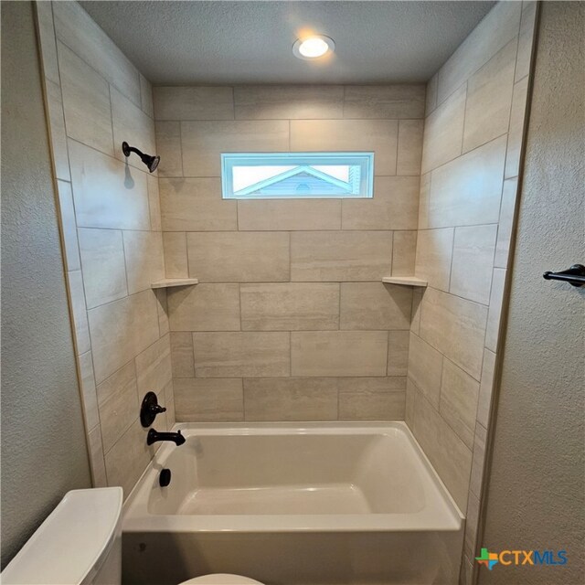 bathroom featuring a textured ceiling, toilet, and tiled shower / bath