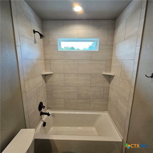 bathroom with a textured ceiling and tiled shower / bath combo