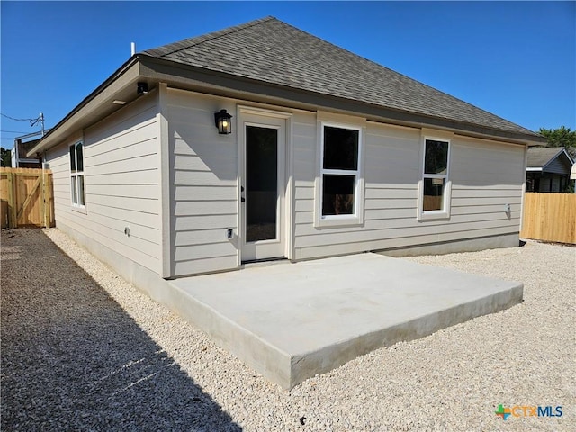 rear view of property featuring fence, a patio area, and a shingled roof