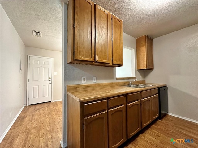 kitchen featuring butcher block countertops, dishwasher, sink, light wood-type flooring, and a textured ceiling