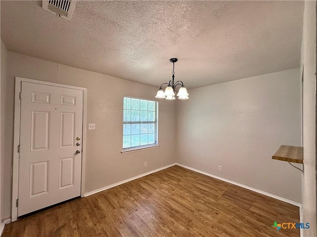 unfurnished dining area featuring hardwood / wood-style floors, a textured ceiling, and a chandelier