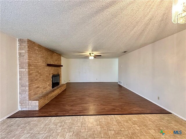 unfurnished living room with wood-type flooring, ceiling fan with notable chandelier, a fireplace, and a textured ceiling