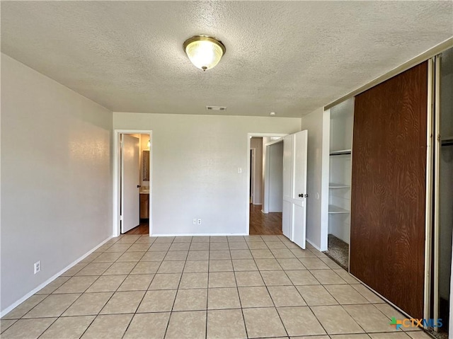 unfurnished bedroom featuring a textured ceiling, a closet, and light tile patterned floors