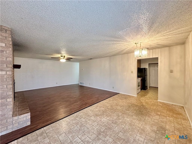 spare room with a brick fireplace, ceiling fan with notable chandelier, a textured ceiling, and light wood-type flooring