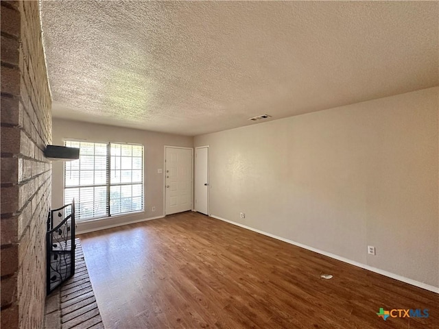 unfurnished living room featuring hardwood / wood-style floors, a brick fireplace, and a textured ceiling