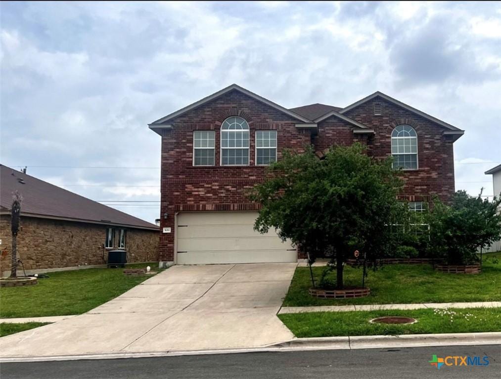 traditional-style house with brick siding, an attached garage, a front yard, and concrete driveway
