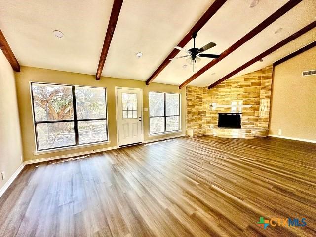 unfurnished living room featuring lofted ceiling with beams, ceiling fan, visible vents, a fireplace, and wood finished floors