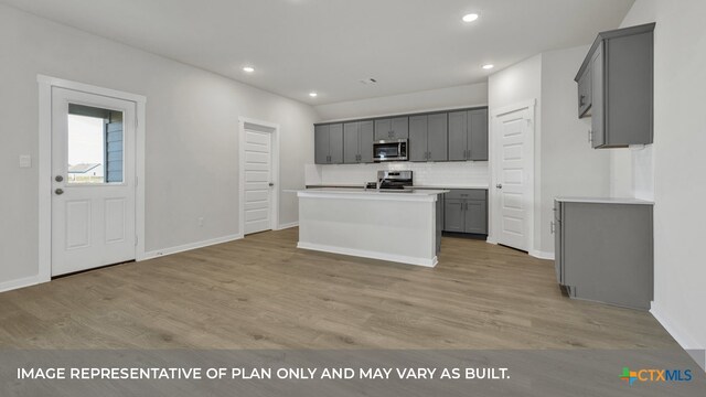 kitchen featuring tasteful backsplash, a kitchen island with sink, gray cabinets, light wood-type flooring, and appliances with stainless steel finishes