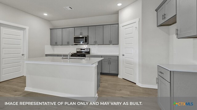 kitchen with a kitchen island with sink, appliances with stainless steel finishes, gray cabinetry, and light hardwood / wood-style flooring