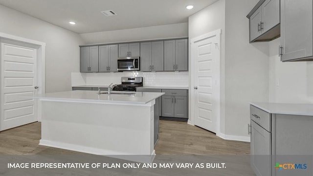 620 Radley Rd, Lockhart, TX 78644 - kitchen featuring appliances with stainless steel finishes, gray cabinetry, light wood finished floors, backsplash, and recessed lighting