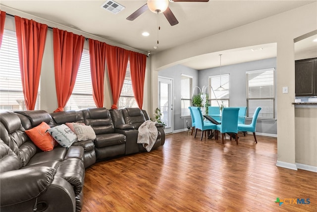 living room with wood finished floors, baseboards, a ceiling fan, visible vents, and arched walkways