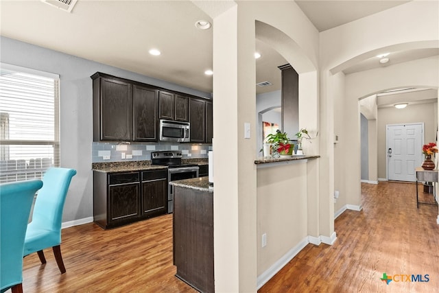 kitchen with arched walkways, light wood-style flooring, stainless steel appliances, and backsplash