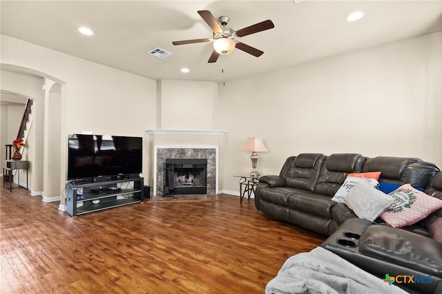 living area featuring a ceiling fan, wood finished floors, visible vents, arched walkways, and a high end fireplace