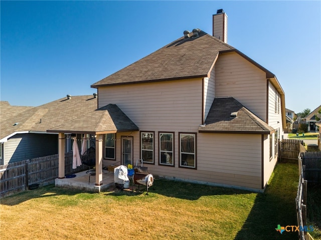 rear view of house with fence, roof with shingles, a chimney, a yard, and a patio area