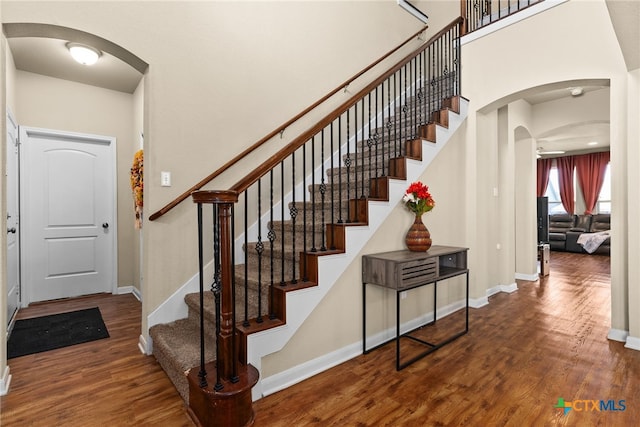 staircase featuring arched walkways, a high ceiling, baseboards, and wood finished floors