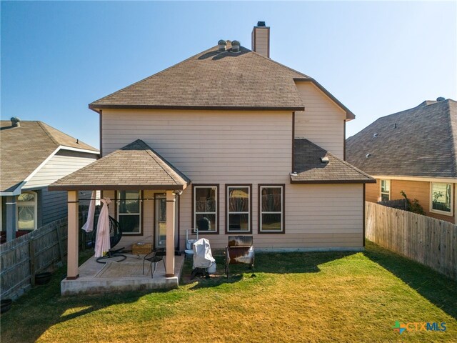 back of house featuring a yard, a patio area, a fenced backyard, and a shingled roof