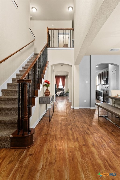 entrance foyer with baseboards, stairs, a towering ceiling, wood finished floors, and arched walkways