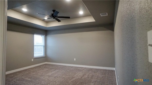 carpeted empty room with a raised ceiling and ceiling fan