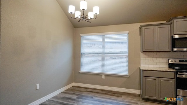 kitchen featuring tasteful backsplash, an inviting chandelier, vaulted ceiling, appliances with stainless steel finishes, and light hardwood / wood-style floors